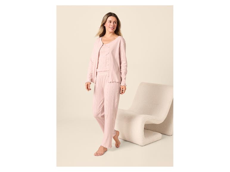 Femme en pyjama rose clair avec un cardigan et un pantalon, debout à côté d'une chaise.