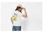 Femme en t-shirt blanc avec citrons et texte 'La Dolce Vita' au dos, casquette beige.