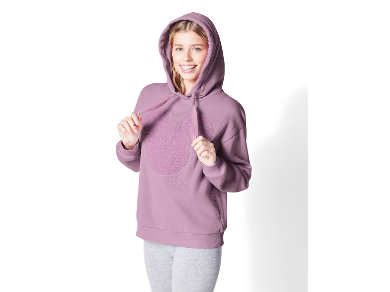 Jeune femme en sweat à capuche lilas avec motif de tête et pantalon de jogging gris.