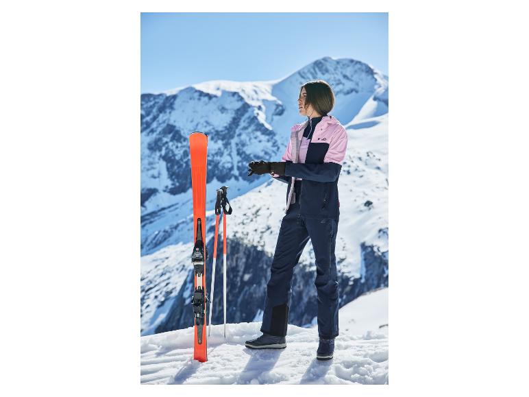 Femme en veste et pantalon de ski, avec skis et bâtons, sur une montagne enneigée.