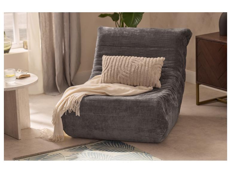 Fauteuil de sol en velours gris avec coussin et plaid crème, à côté d'une table d'appoint.