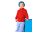 Garçon en col roulé rouge avec boussole et pantalon bleu, appuyé sur un bloc bleu.