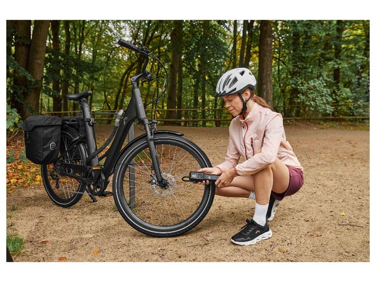 Femme en casque gonflant le pneu d'un vélo électrique CRIVIT avec une pompe à air portable.
