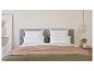 Cadre de lit gris dans une chambre avec une couverture beige et des draps verts.