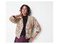 Femme souriante portant un cardigan beige en tricot et un pantalon en cuir bordeaux.