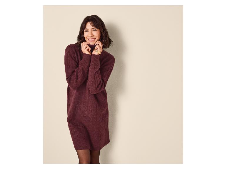 Femme souriante en robe pull bordeaux, collants noirs, posant sur fond clair.