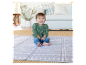 Bébé souriant sur un tapis de jeu gris à motifs géométriques.
