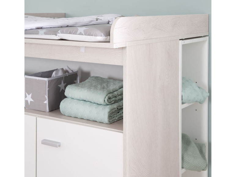 Une commode avec un matelas à langer, un tiroir et des étagères ouvertes.