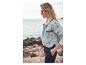 Une femme porte une veste en jean et un pantalon près de la mer.