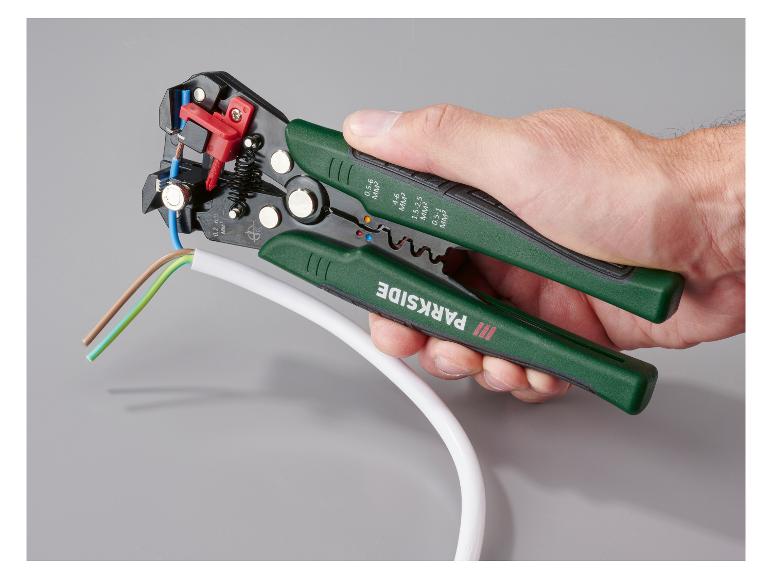 Pince à dénuder automatique Parkside en main, dénudant un câble blanc.