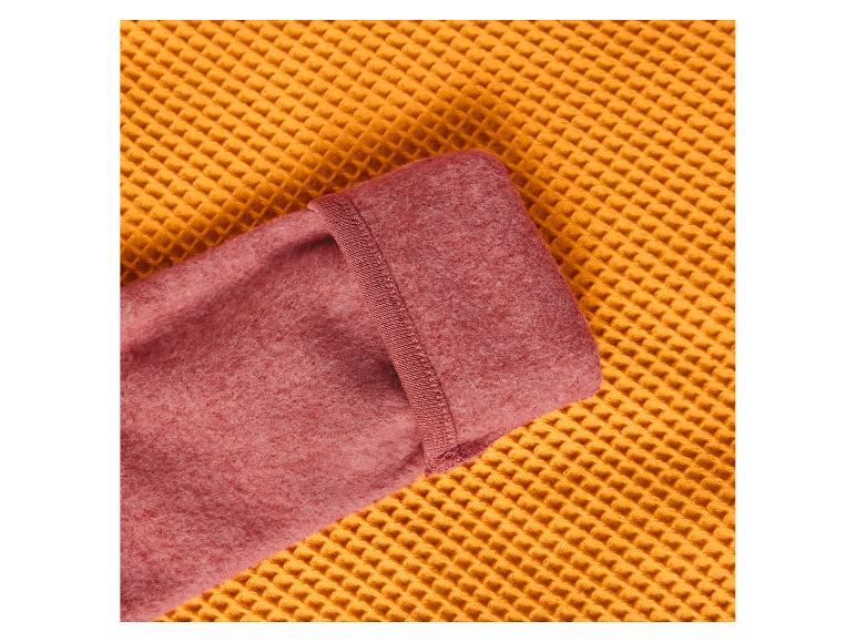 Gros plan d'une couverture polaire rose pliée sur une surface jaune gaufrée.