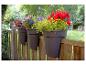 Trois jardinières grises avec des fleurs colorées suspendues à une clôture en bois.