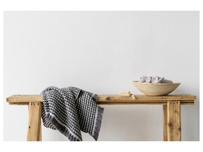 Serviette tissée et accessoires de bain sur un banc en bois rustique contre un mur blanc
