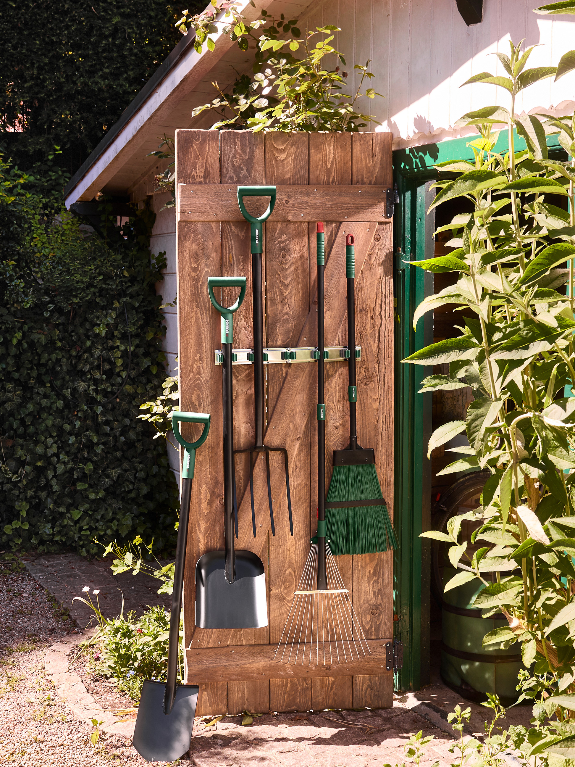 Outils de jardin: pelles, fourches, râteaux et balai, accrochés à une porte de cabanon en bois.