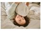 Femme souriante allongée sur le dos dans un lit avec une couette et un oreiller beiges.
