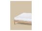 Matelas blanc sur un cadre de lit en bois clair sur fond beige.
