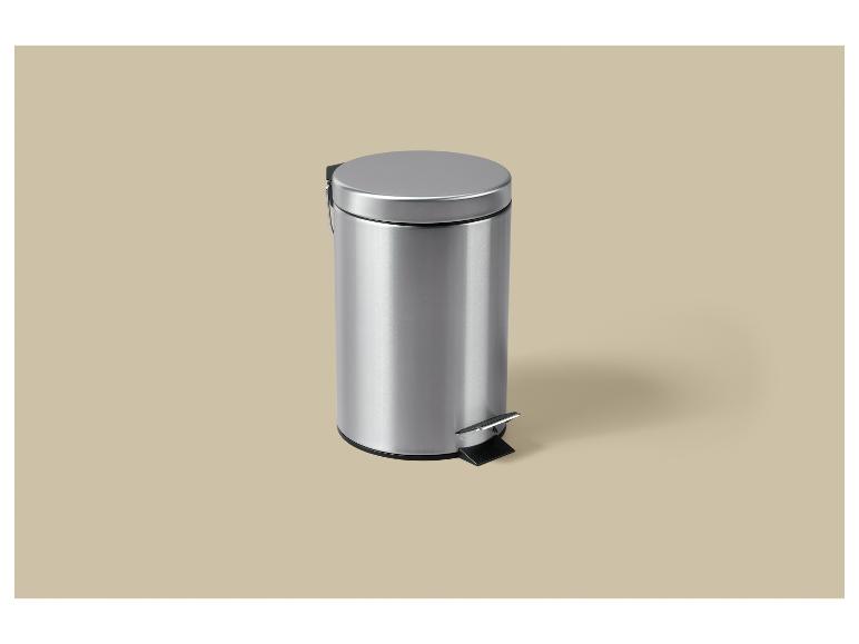 Une poubelle à pédale argentée avec couvercle sur un fond beige.