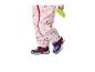 Enfant en combinaison de pluie rose à cœurs et chaussures bleu marine, tenant un jouet vert.