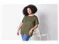 Une femme en t-shirt vert olive et jeans s'appuie contre une chaise blanche.