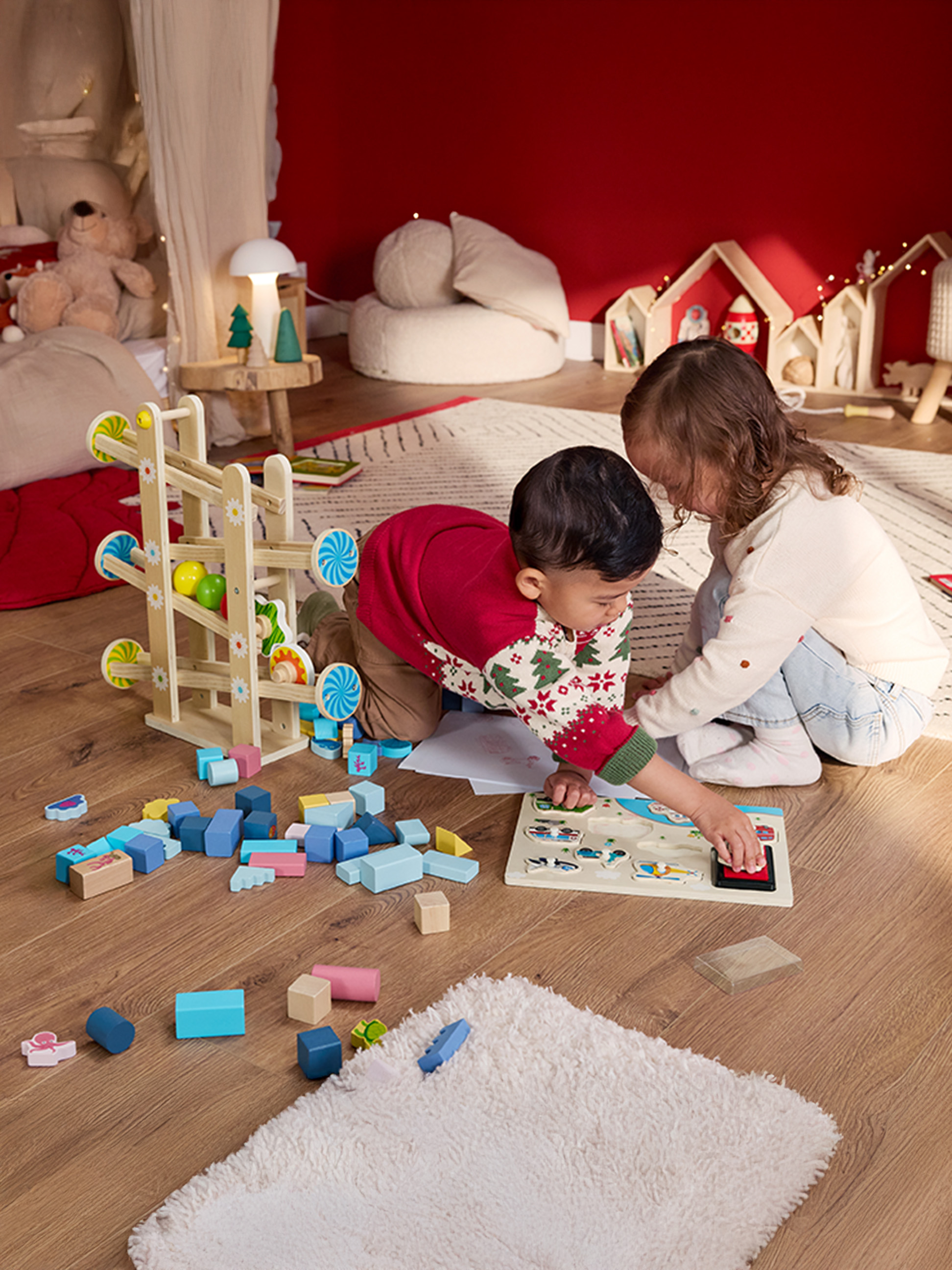 Deux enfants jouent avec des jouets en bois et un circuit de billes sur un parquet.