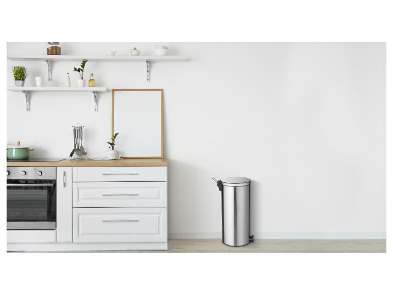 Cuisine moderne avec armoires blanches, plan de travail en bois et poubelle en acier inoxydable.