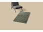 Chaise grise et tapis vert avec motif abstrait de rose sur fond beige.