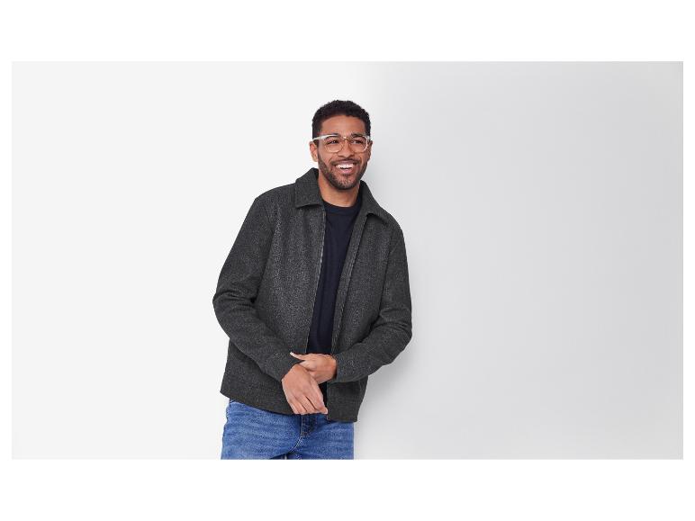 Homme souriant avec des lunettes, portant une veste grise et un jean.