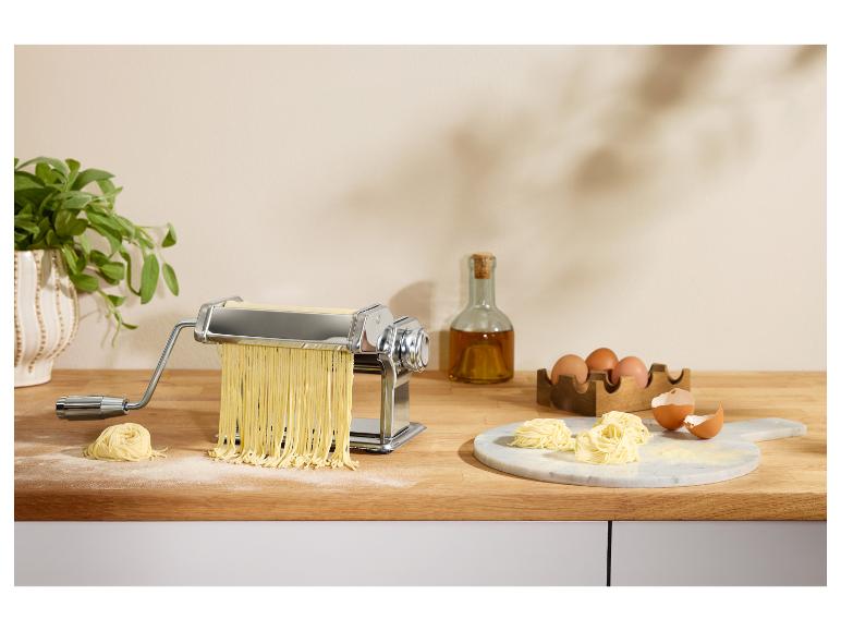 Machine à pâtes avec pâtes fraîches, œufs et huile d'olive sur un comptoir en bois.