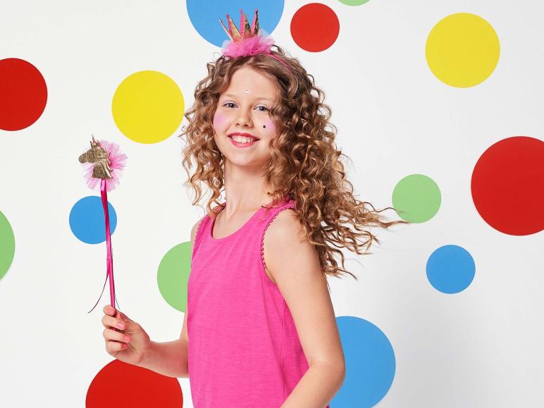Une fille avec un haut rose et une baguette magique licorne devant un fond de points colorés.