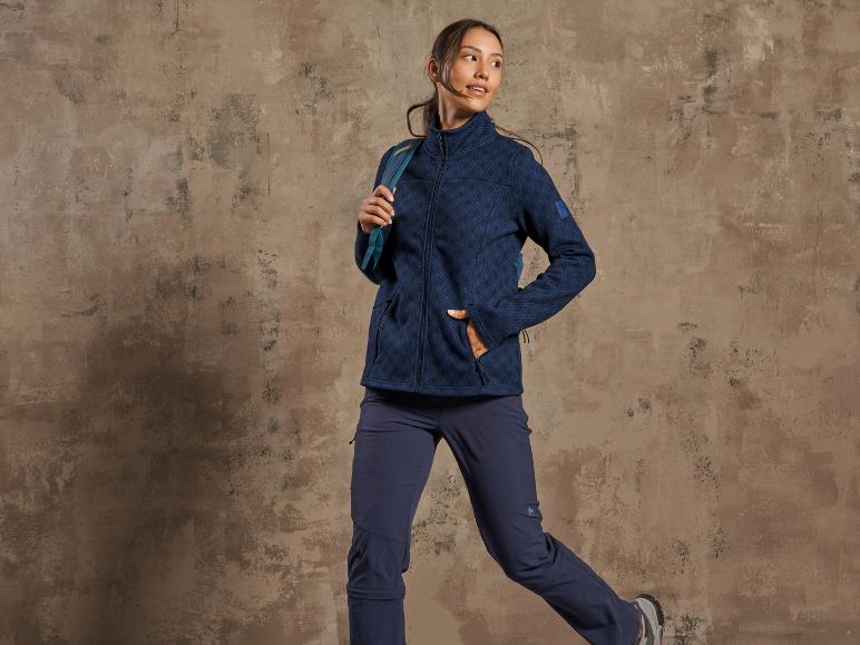 Une femme portant une veste en polaire bleue et un pantalon de randonnée bleu.