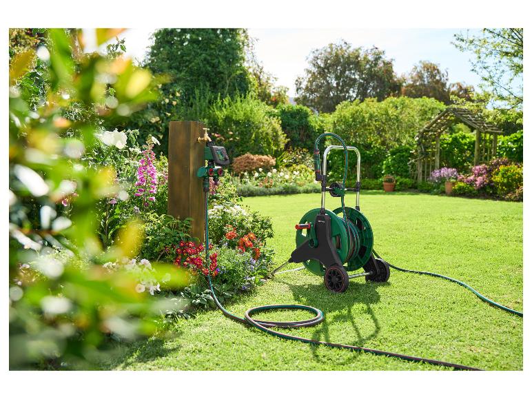 Dévidoir de tuyau Parkside et programmateur d'arrosage sur poteau en bois dans un jardin fleuri.