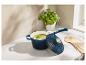 Casserole bleue avec couvercle, remplie de soupe verte, sur un comptoir en marbre avec un plant de basilic.