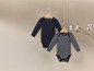 Deux bodies bébé, un rayé et un noir uni, suspendus à des cintres en bois.