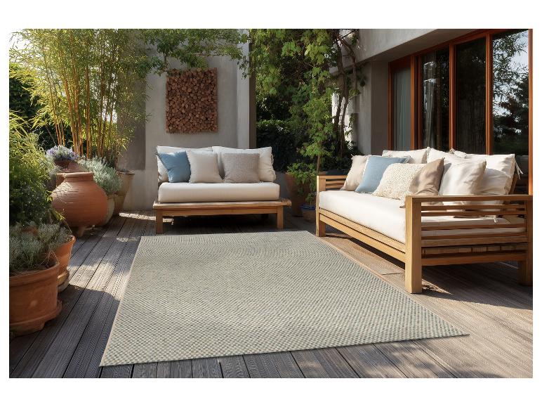 Terrasse avec mobilier de jardin en bois, coussins clairs et tapis à motifs.