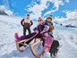 Deux enfants sur une luge dans la neige, avec un adulte en arrière-plan.