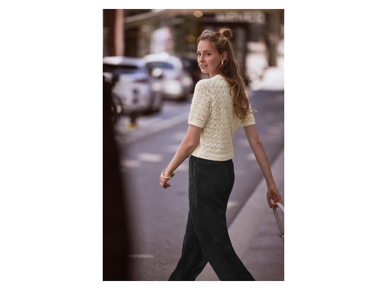 Femme marchant dans la rue, vêtue d'un pull jaune clair et d'un pantalon noir.