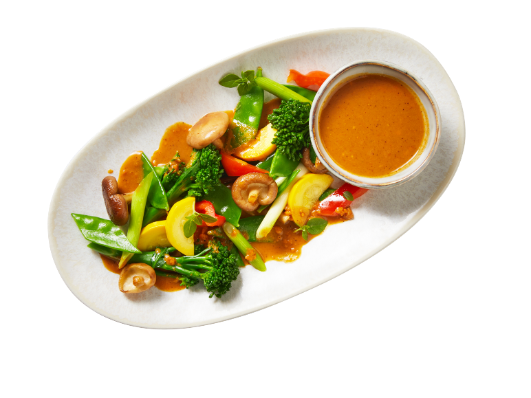 Légumes sautés colorés avec champignons et sauce aux cacahuètes sur une assiette ovale.