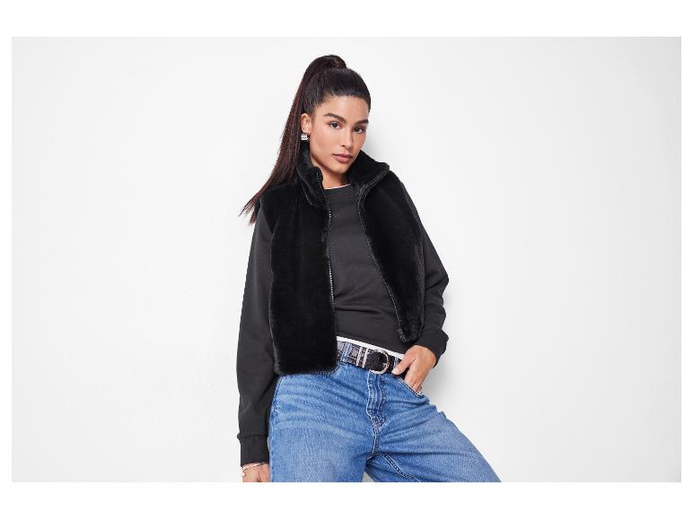 Femme en veste en fausse fourrure noire, haut noir et jean bleu avec ceinture