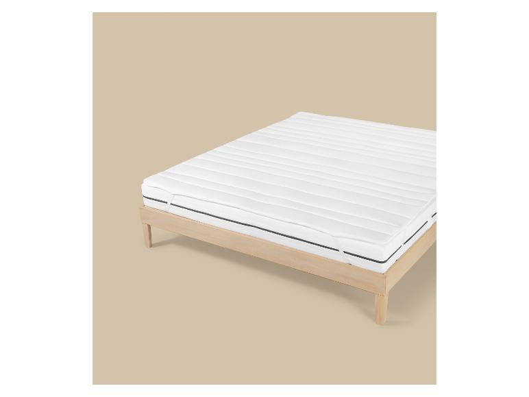 Cadre de lit en bois avec matelas blanc et surmatelas, sur fond beige.