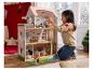 Une jeune fille joue avec une grande maison de poupée en bois à plusieurs étages et accessoires.