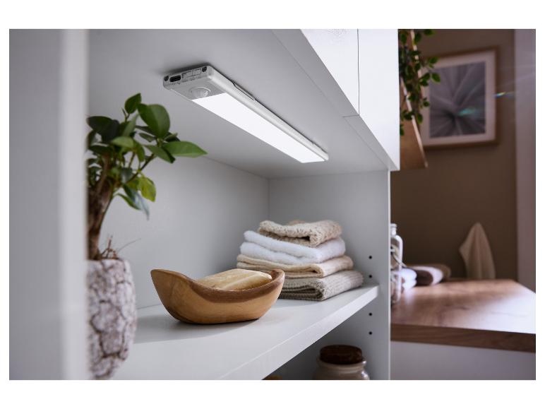Un éclairage de placard LED avec capteur de mouvement monté sous une armoire blanche, avec serviettes et savon.