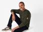 Un homme avec un pull vert, un pantalon noir et des baskets blanches.