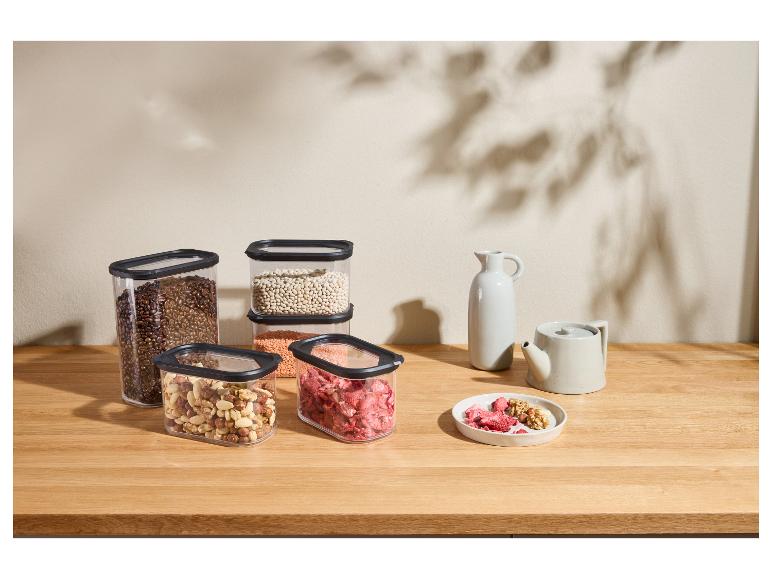 Récipients alimentaires transparents avec grains de café, noix, lentilles et fruits secs sur une table en bois.