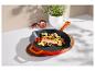 Poêle en fonte orange avec saumon, légumes et herbes sur un dessous de plat en bois.