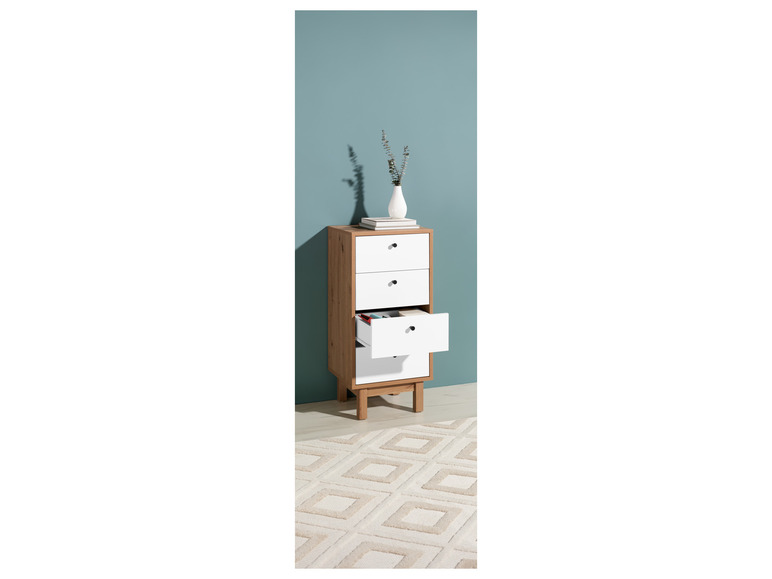 Une commode blanche avec des pieds en bois sur un tapis à motif géométrique.