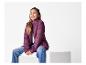 Une jeune fille souriante assise sur un cube blanc, portant une veste matelassée violette et un jean.