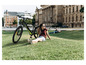 Une femme est allongée sur l'herbe à côté d'un vélo électrique noir de la marque Fischer