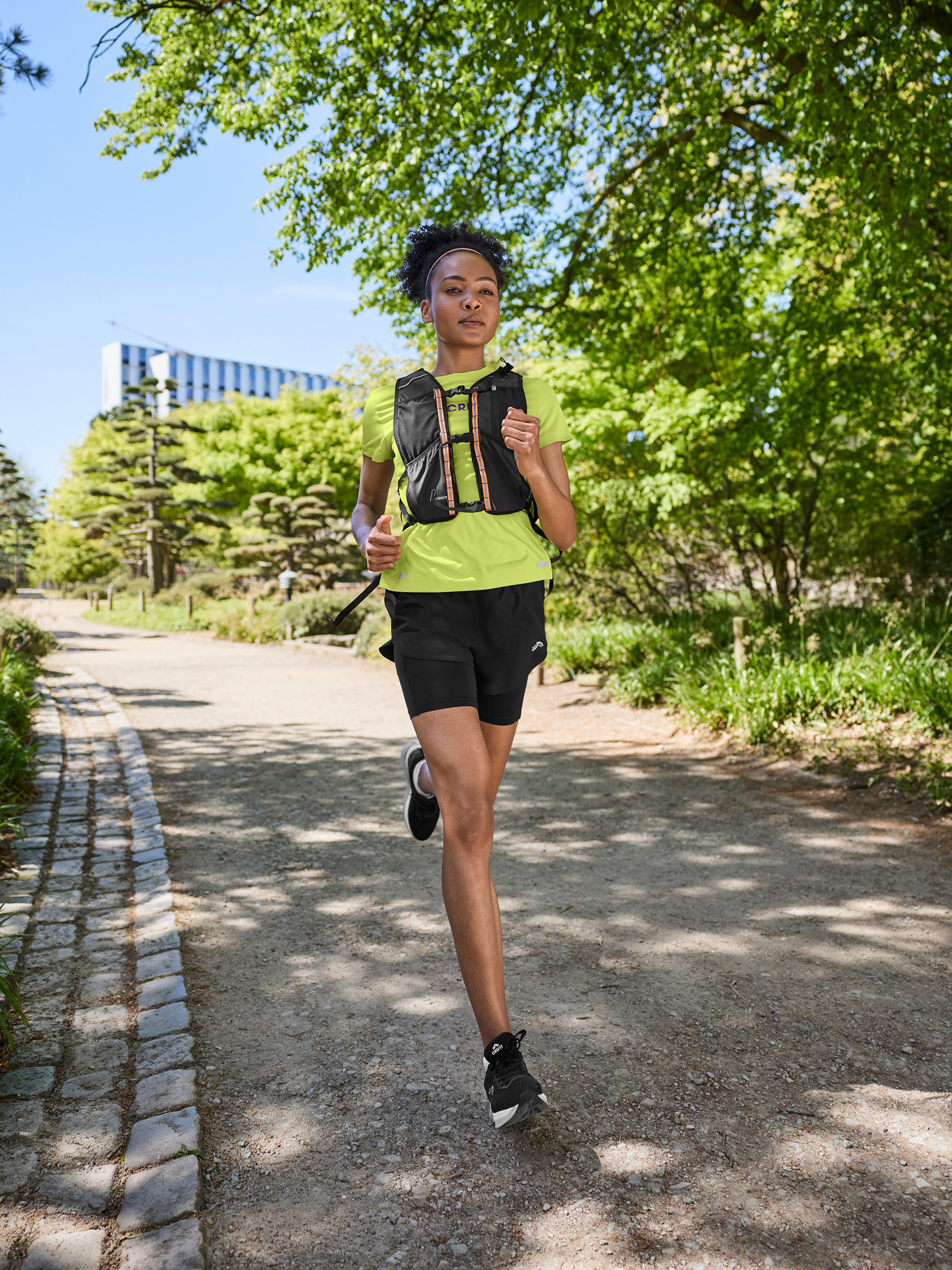 Femme en t-shirt de sport, short et gilet de course, courant sur un chemin de terre.