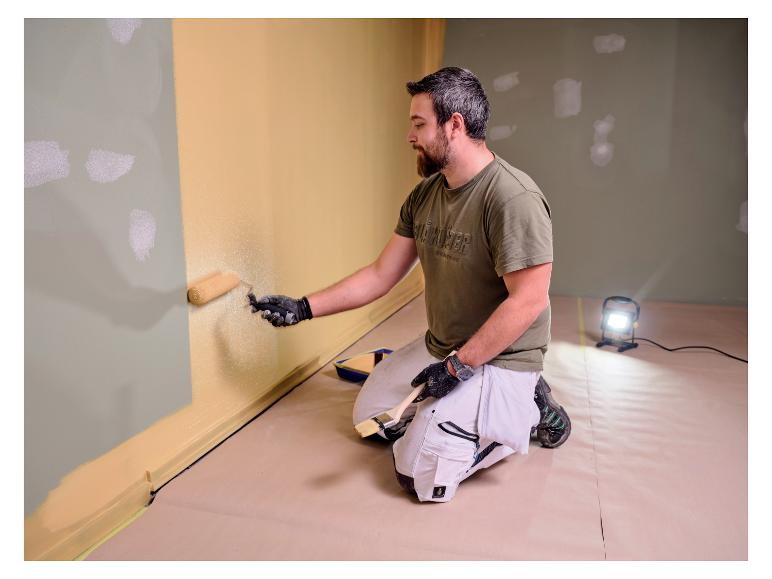 Homme peignant un mur, éclairé par la lampe de travail LIVARNO® »The Painter«.
