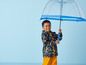 Un garçon portant un imperméable à imprimé marin et tenant un parapluie transparent.